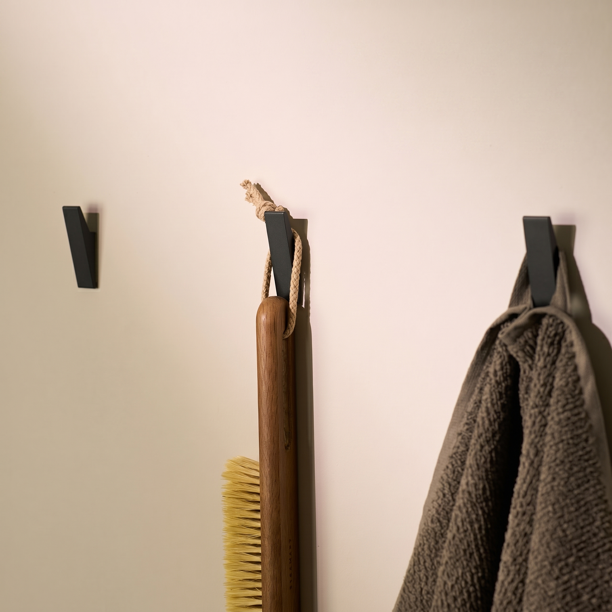 Black adhesive wall hooks holding a towel and brush