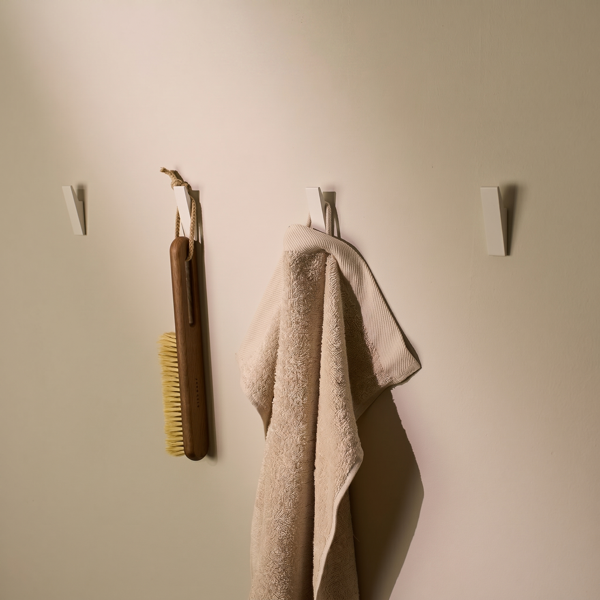 White adhesive wall hooks holding a towel and brush on a wall